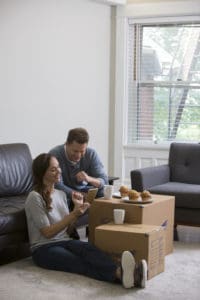 young couple taking a break from packing their living room, using a box as a table for their breakfast muffins - United Van Lines®